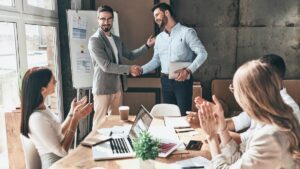 Image of a leader, supervisor, boss, manager shaking hands with individual in front of employees, subordinates, followers.