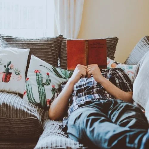 Person laying on the couch reading a book in their comfort zone.