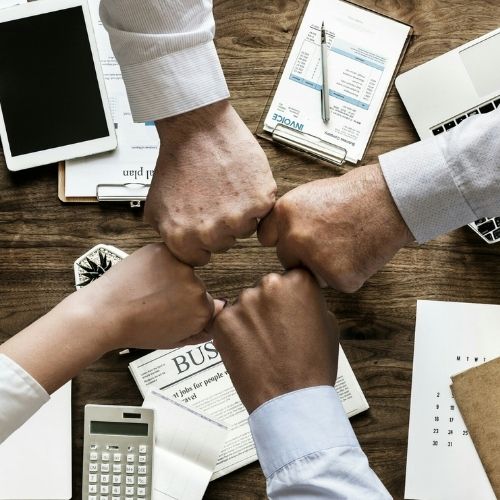 Image of four people fist-bumping after a successful meeting for tips on how to run effective staff meetings.