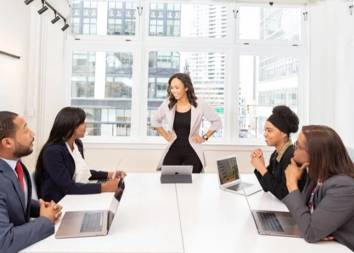 A leader standing at the head of a table discussing the importance of teamwork in the workplace.