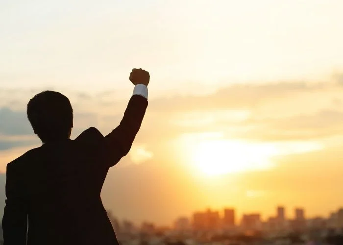 Man holding his hand in the air staring at a city off in the distance.