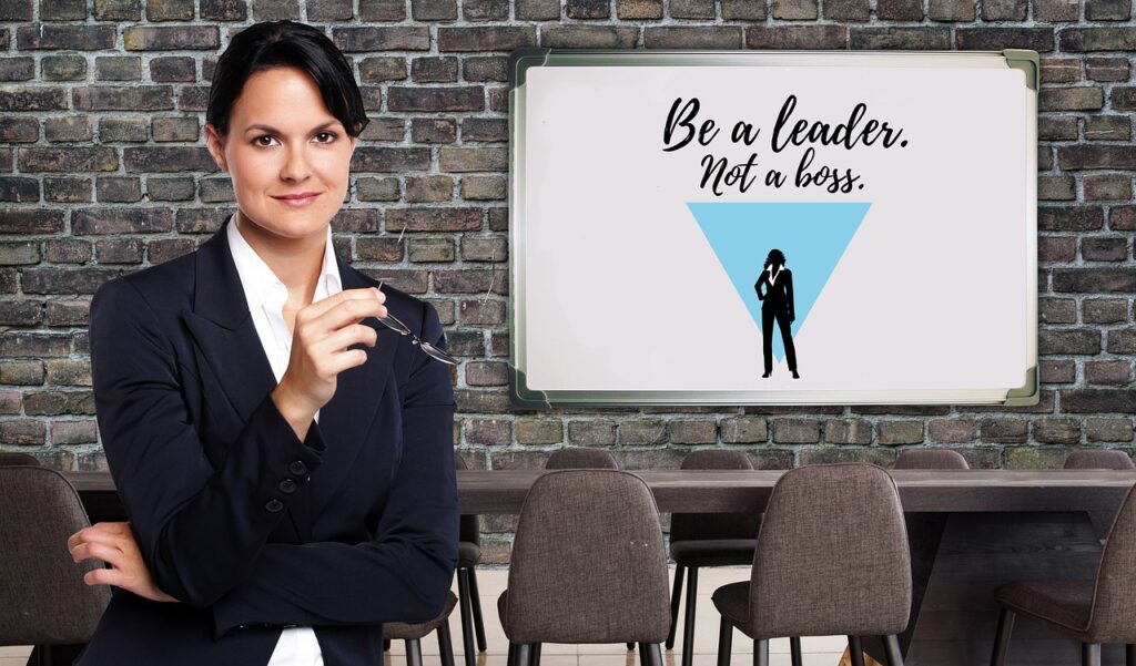 A business woman with a white board that says be a leader not a boss displaying one of the 12 qualities of a good leader.