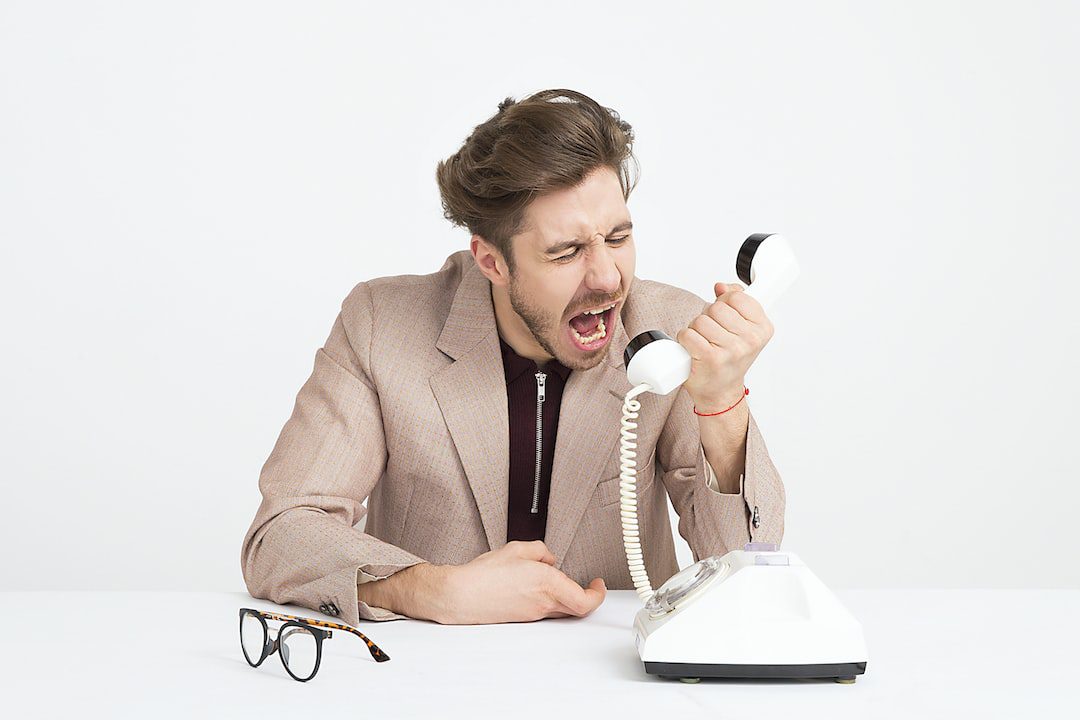 Person yelling into the receiver of a phone to show the wrong kind of communication in the workplace.