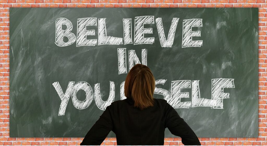 A person looking at a chalkboard with the words believe in yourself written on it for maintaining a positive attitude in the workplace.